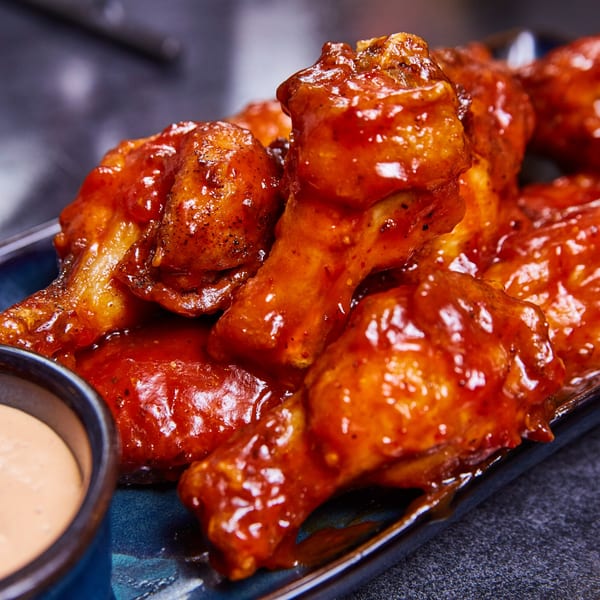 Close-up of RocketFuel Wings, a plate of glistening red-sauced chicken wings with a side of dipping sauce.